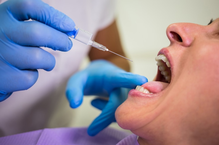Patient with mouth open receiving lidocaine injection from dentist